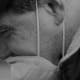 A profile of a man with cerebral palsy. He is wearing a white mask covering his mouth and his eyes are crinkled in a smile.